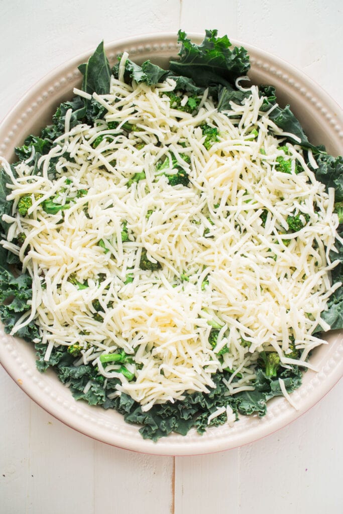 shredded cheese on top of broccoli in baking dish.