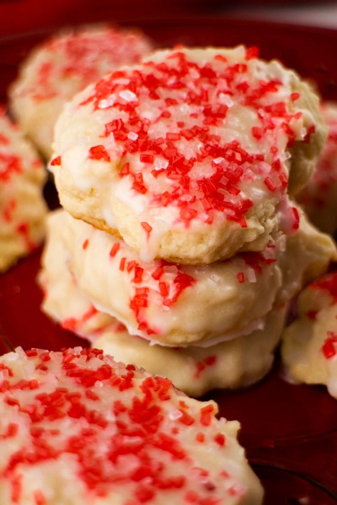 stack of cream cheese sugar cookies with white icing and red sprinkles on red plate