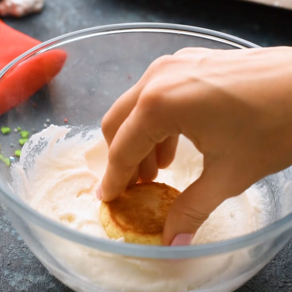 hand dipping cookie into frosting bowl. 