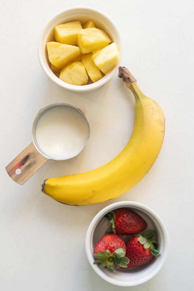 pineapple, banana, strawberries and milk on table. 