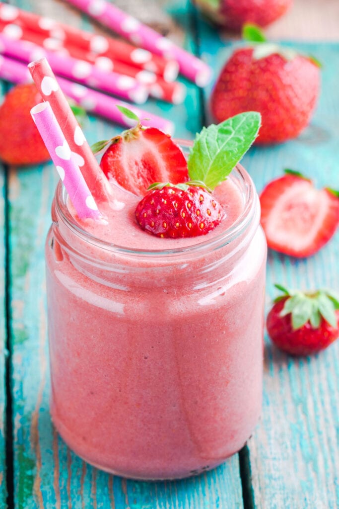 smoothie in glass with strawberries surrounding it.