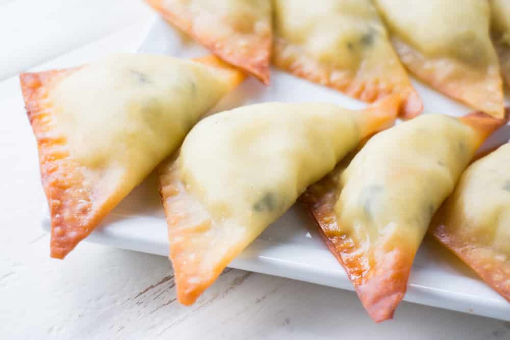 EASY BAKED Three Cheese Ravioli is one of my family's favorite meals! This homemade recipe uses wonton wrappers for the ravioli to make it faster and is filled with ricotta, mozzarella and Parmesan cheese! Instructions include how to make and bake immediately or freeze for frozen ravioli. 
