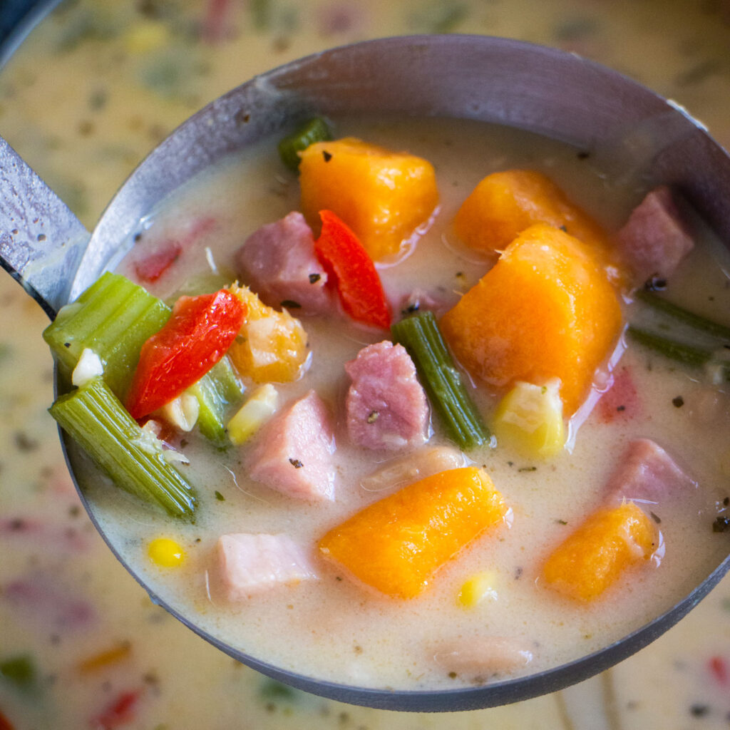 large spoon lifting creamy ham and potato soup out of slow cooker.