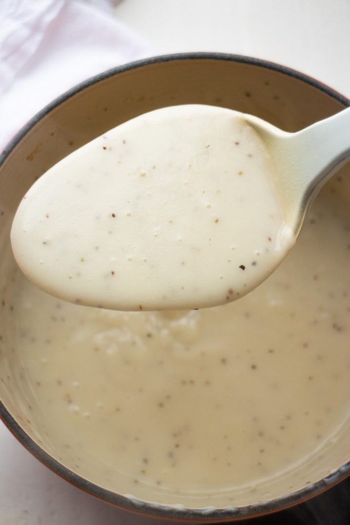 cream sauce in spoon above saucepan.