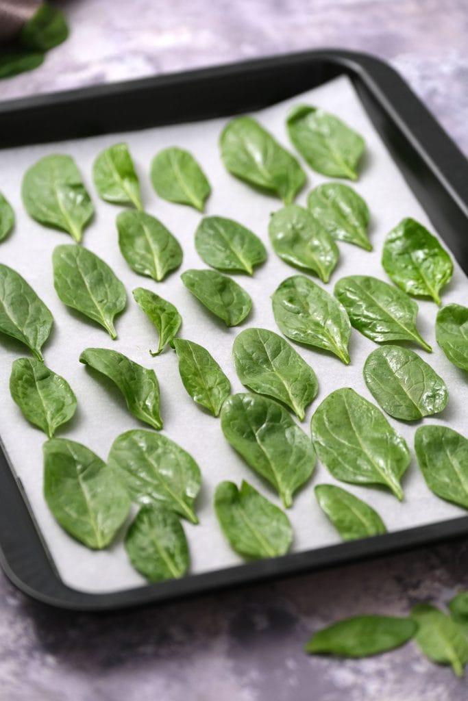 spinach leaves on parchment paper on baking sheet