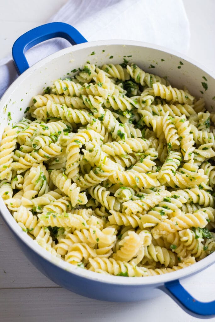 pasta with parmesan and parsley in large blue pot on table.