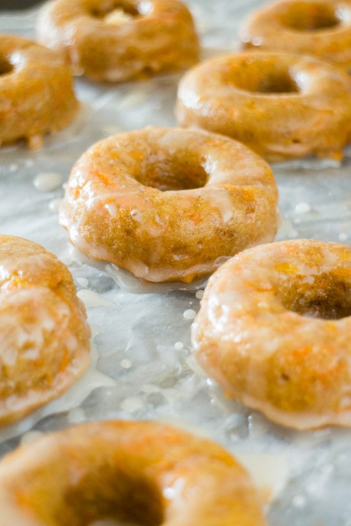side view of glazed carrot donuts on baking sheet.