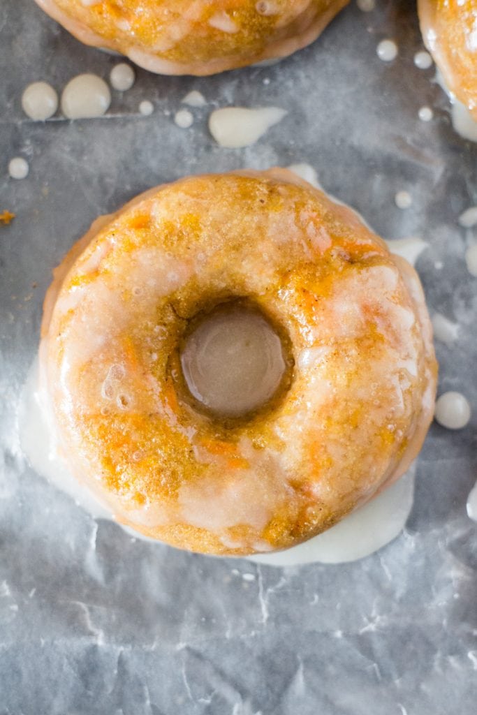 baked carrot donut with glaze on parchment paper on baking sheet.