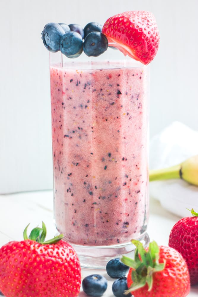 glass filled with a smoothie with blueberries and strawberries on top.