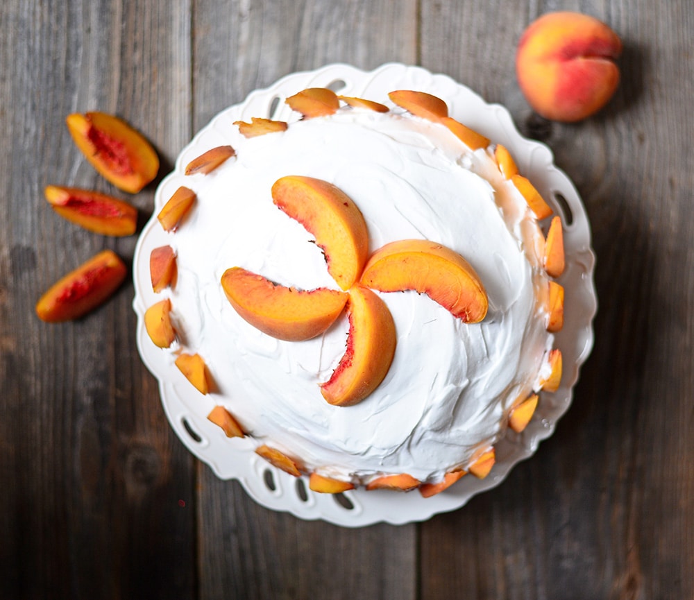 EASY to make Peach Cake with Vanilla Frosting recipe. The cake is so moist and made with fresh peaches inside and for decoration on top. This cake is made with two 8 inch cake pans layered together.  It's the perfect cake for Summer peach season!