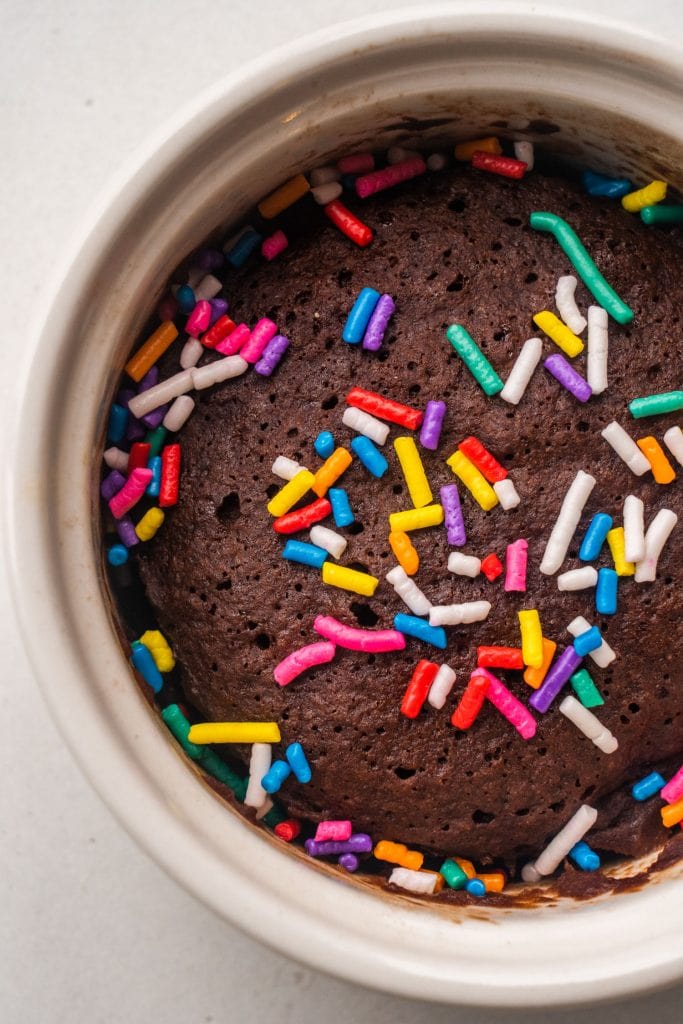 single serving chocolate brownie in white bowl with rainbow sprinkles on top