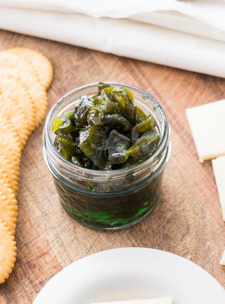 candied jalapenos in glass jar on wood background with crackers