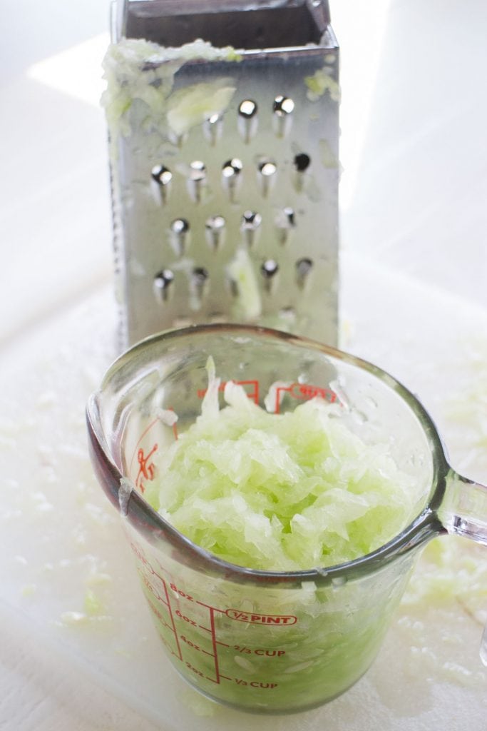grated cucumber in measuring cup with grater behind it