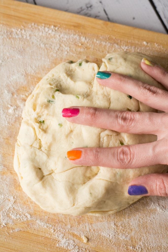 hand with rainbow nails kneading dough on floured surface.