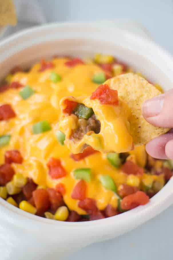 HEALTHY 7 Layer Taco Dip is easy to make with tomatoes, corn, lettuce, pinto refried beans, green pepper, and cheese! Ready in 10 minutes! This Mexican dip is made without cream cheese and ground beef! Serve hot or cold! 