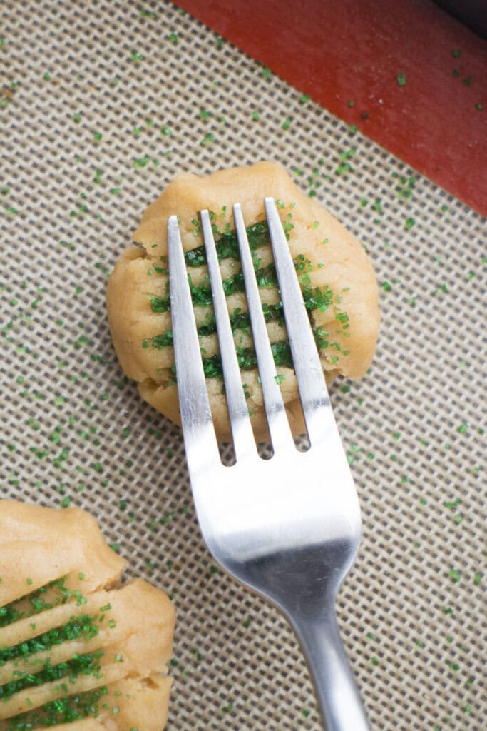 fork pressing down peanut butter cookie on baking sheet.
