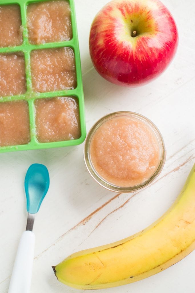 glass jar of baby food on white table with blue spoon