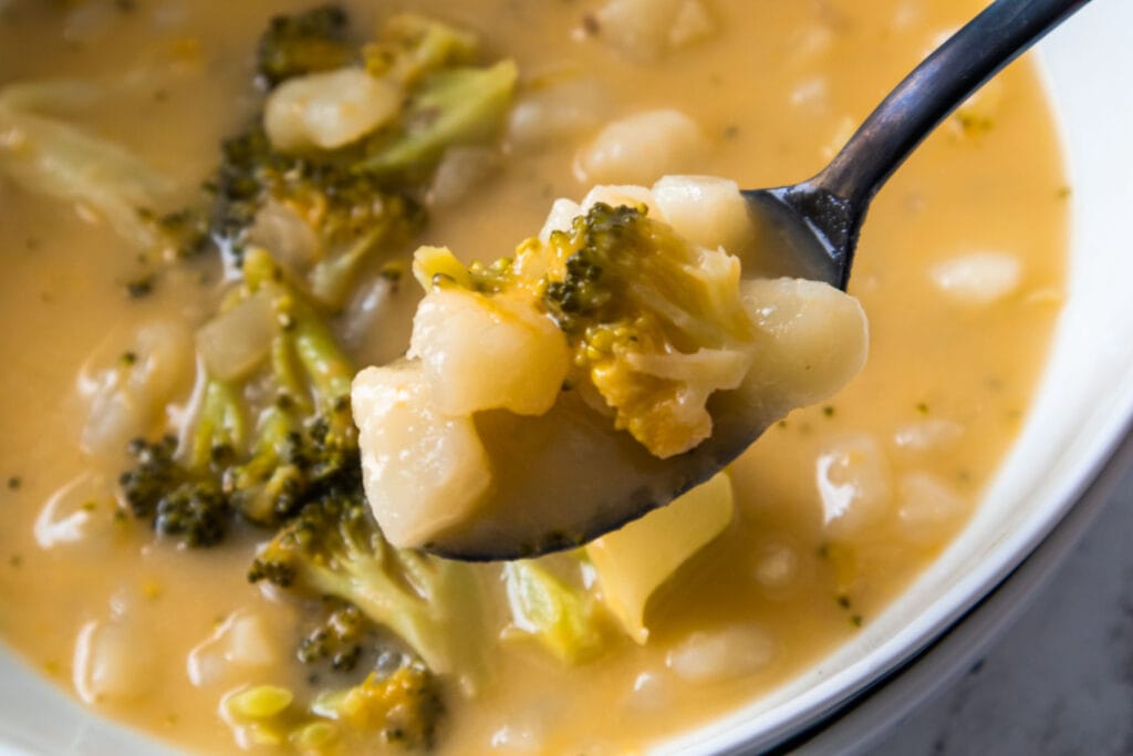 spoon lifting broccoli cheese and potato soup out of bowl. 