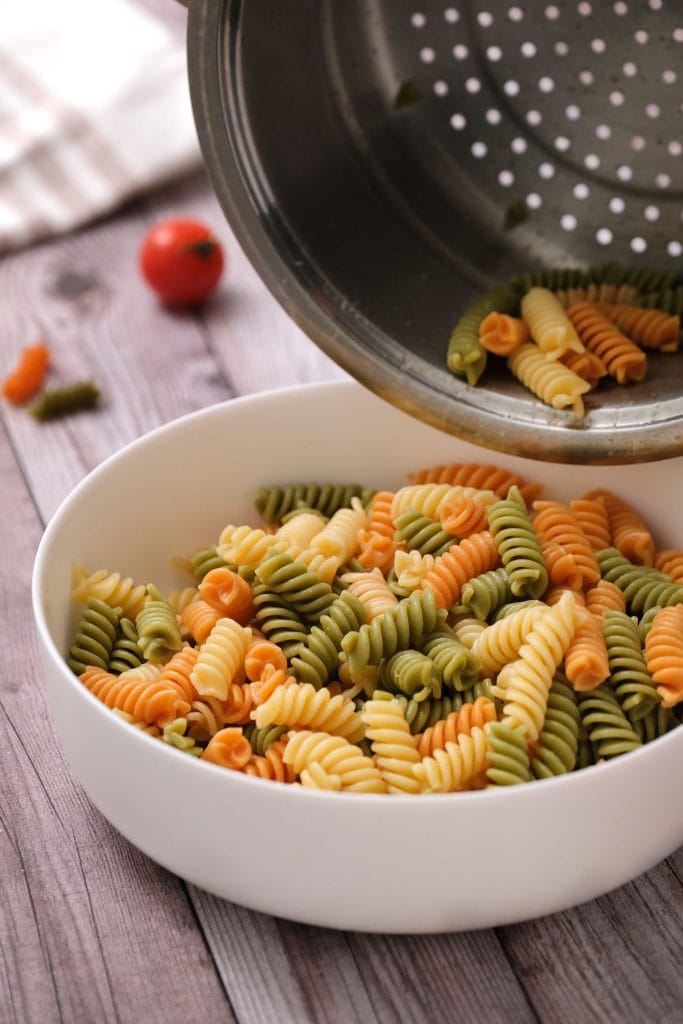 tri color rotini being drained into white bowl