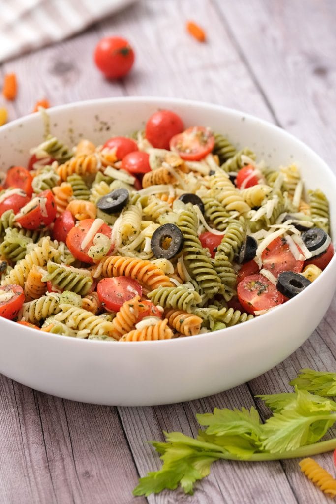 tri color pasta salad with cheese, tomatoes and olives in white bowl