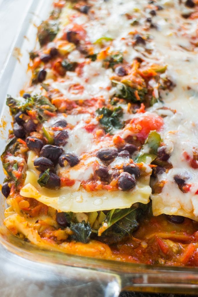 cheesy lasagna with beans, tomatoes and kale in baking dish.