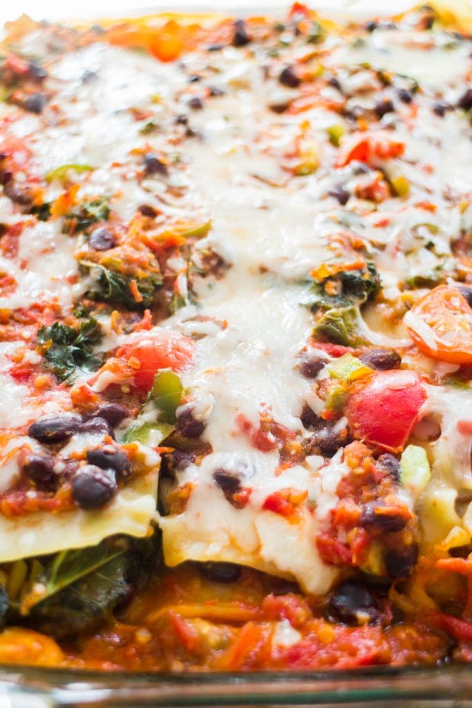 baked lasagna with black beans, peppers, tomatoes and kale in baking dish.