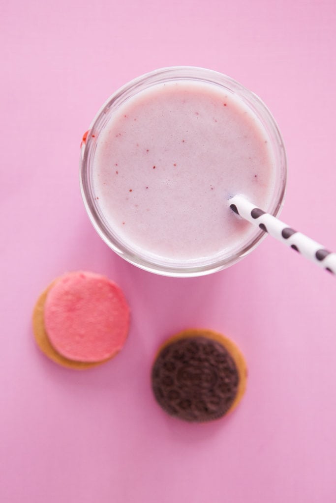 glass of strawberry milk in cup with cookies next to it.