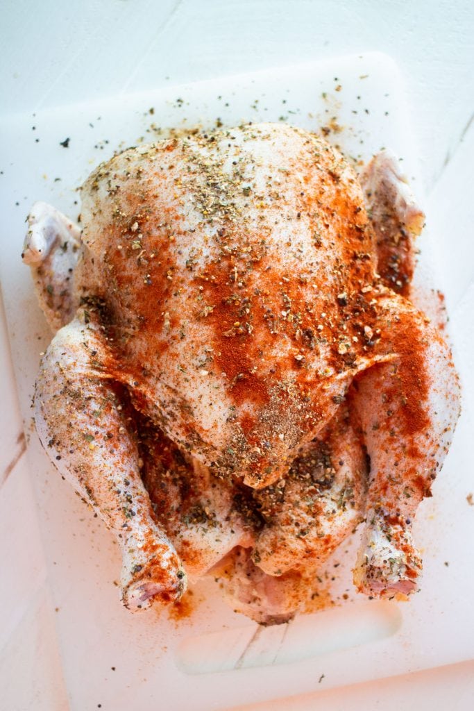 raw whole chicken with poultry seasoning and paprika on top of it