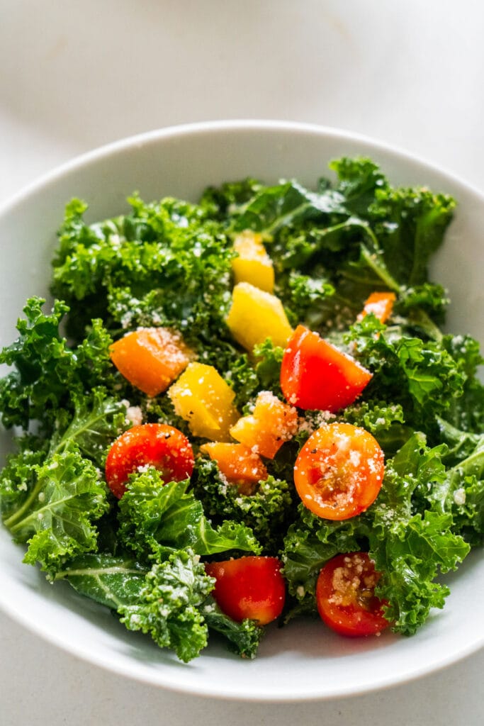 kale salad with cherry tomatoes and peppers in small white bowl.