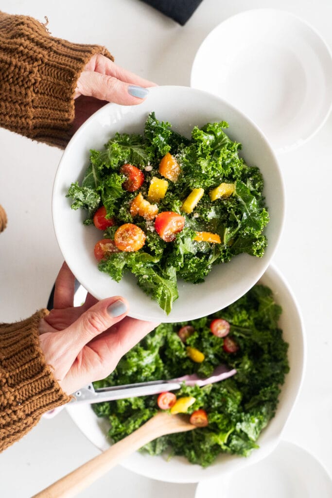 hands holding bowl of kale salad above table.