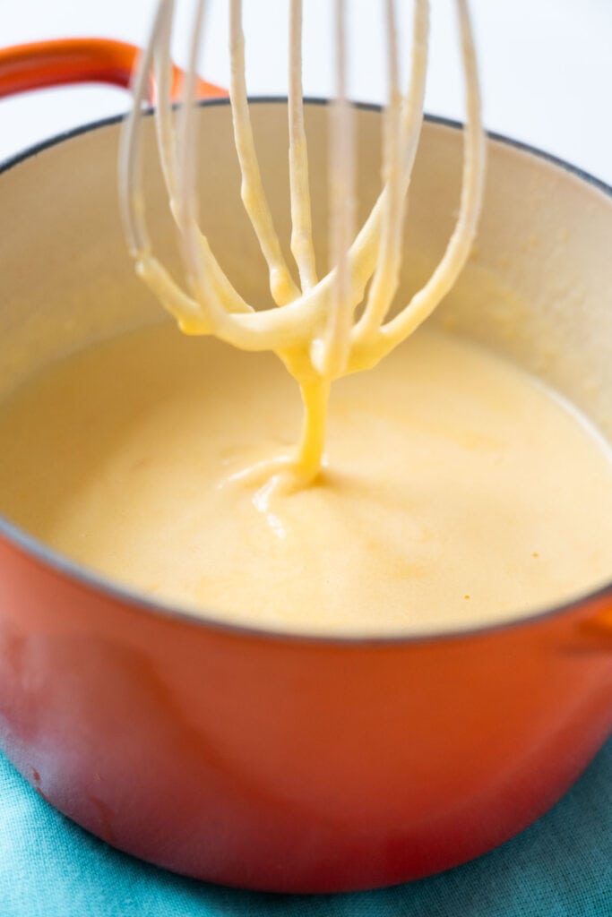 whisk mixing cream sauce in orange saucepan