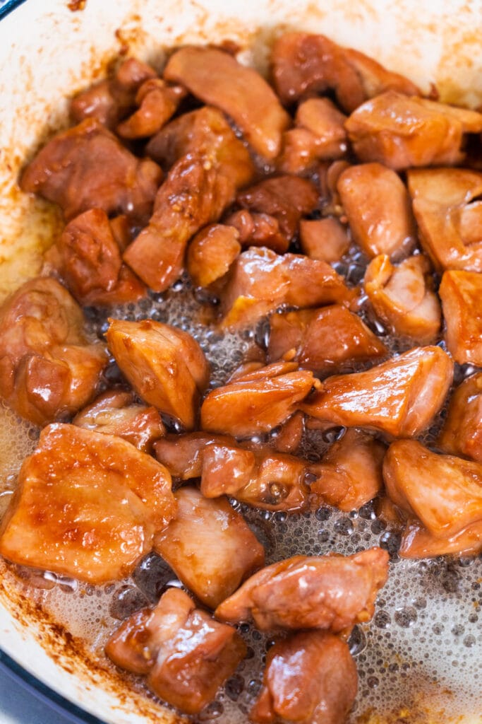 chicken simmering in skillet in brown sauce.