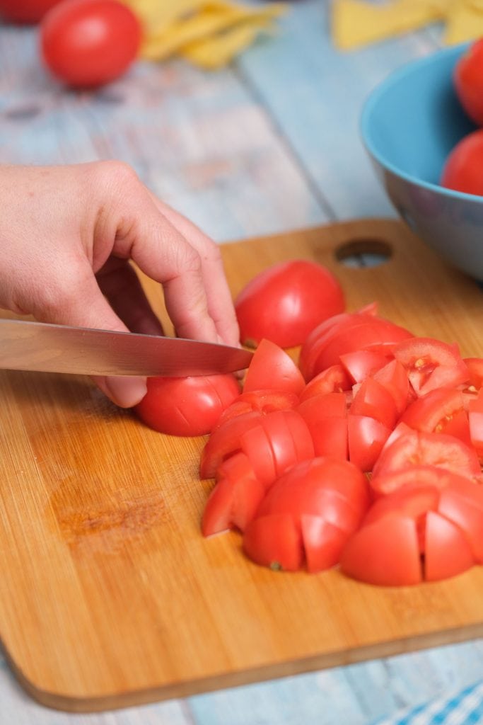 roma tomatoes being chopped up with sharp knife on cutting board