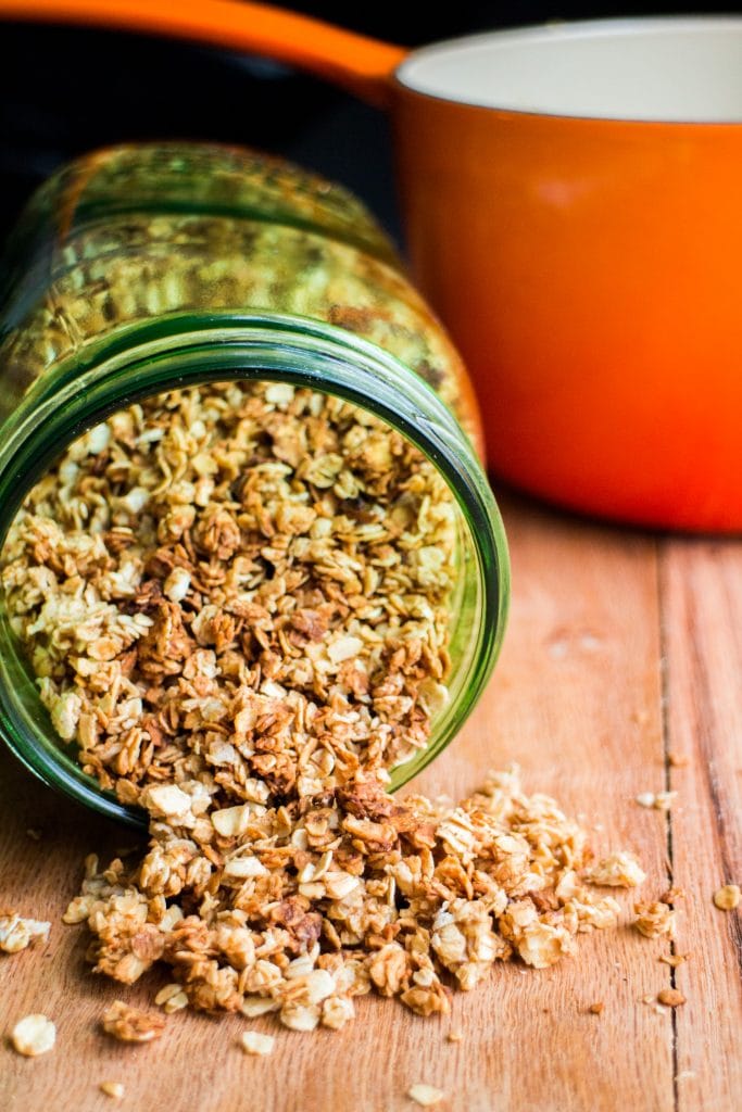 crispy granola coming out of green mason jar on table.