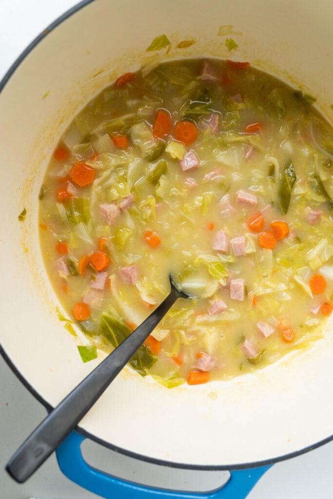 ham and cabbage soup in large pot with spoon.
