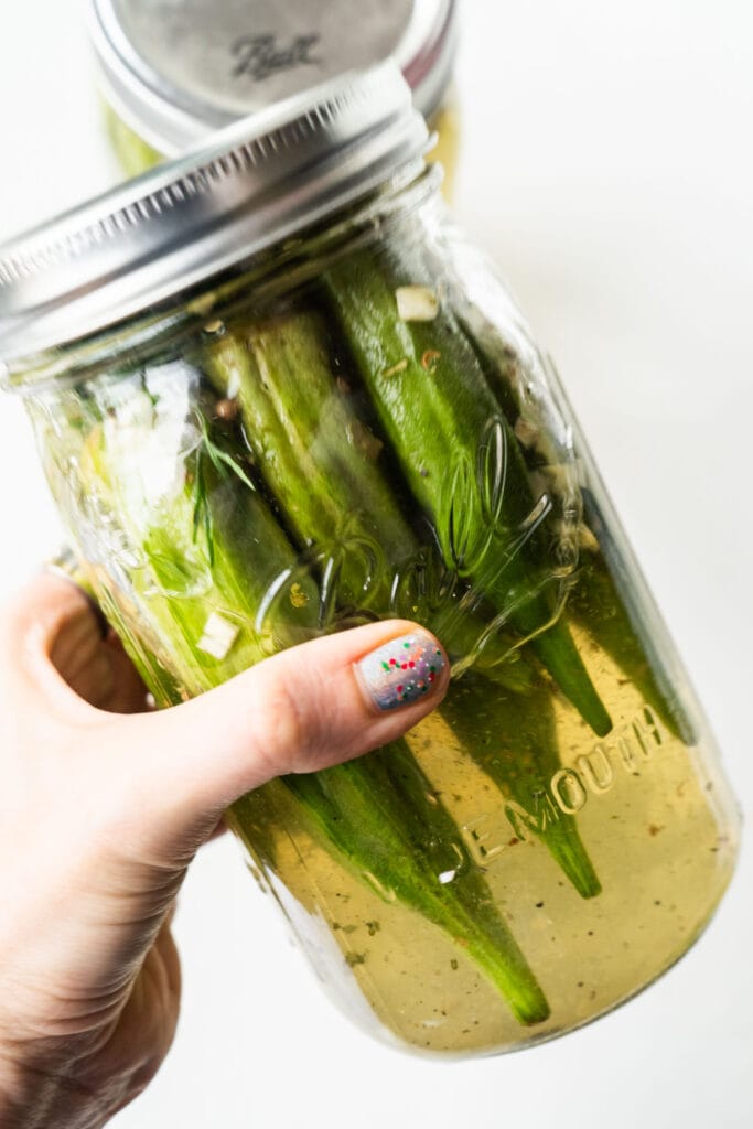 hand shaking mason jar filled with pickled okra.