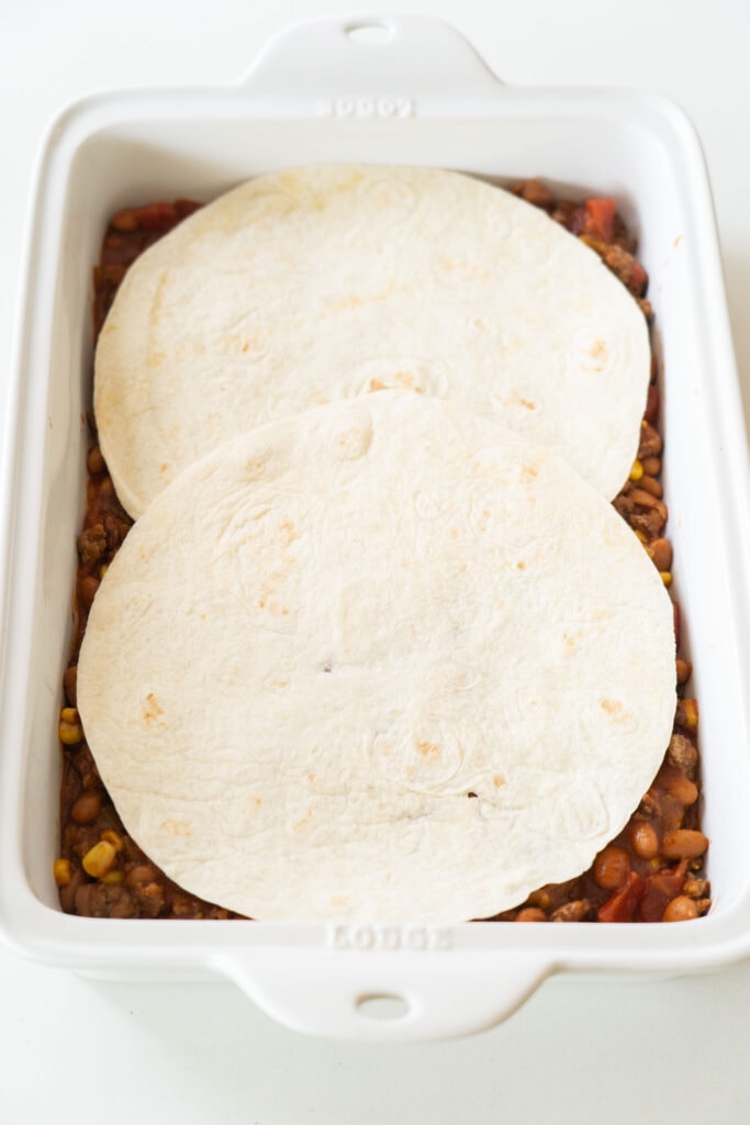 tortillas being layered on top in baking dish.
