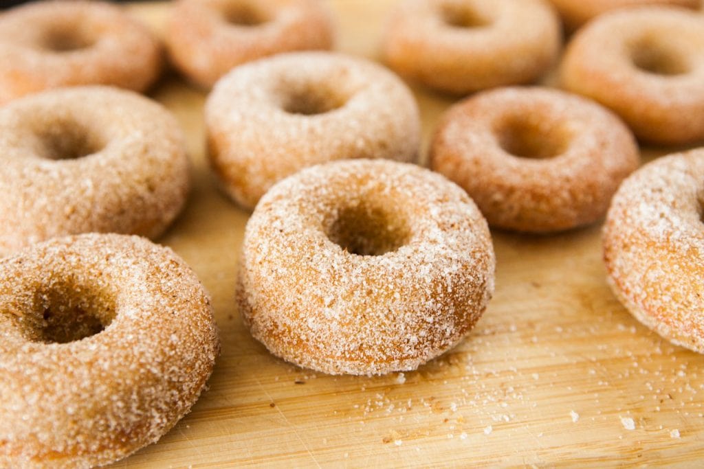 dozen of pumpkin donuts with cinnamon sugar on top on wooden table