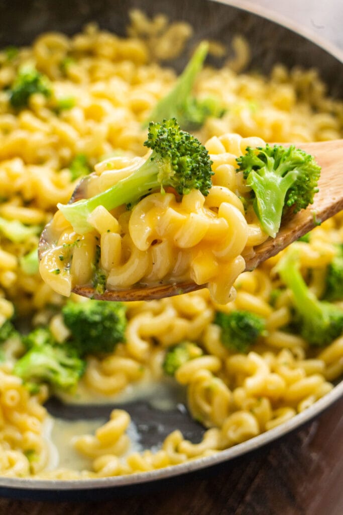 spoon lifting cheesy noodles and broccoli out of pot.
