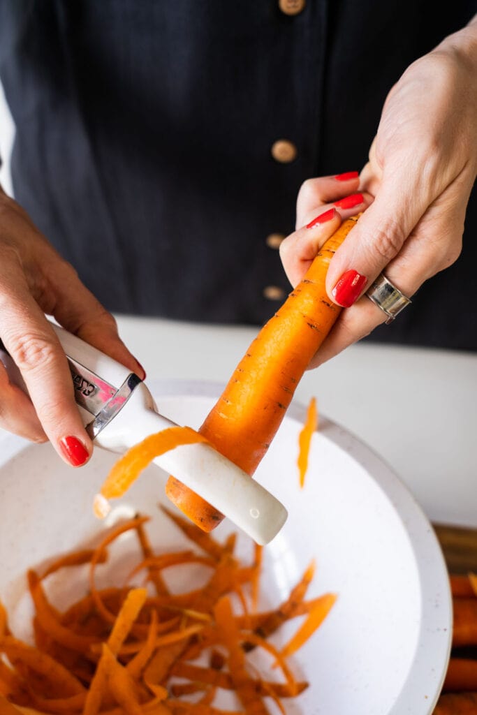 hand peeling carrots into bowl. 