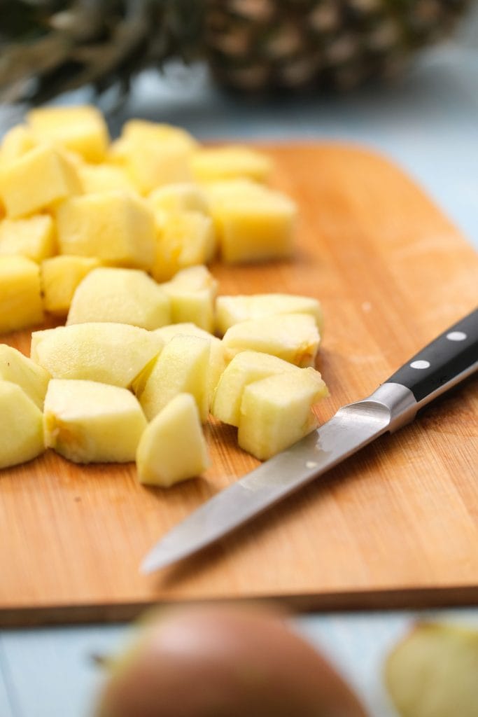 pineapple cubed on cutting board with knife