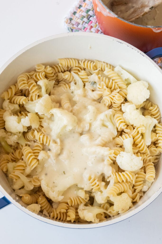 cream sauce poured into the middle of pot with pasta and cauliflower.
