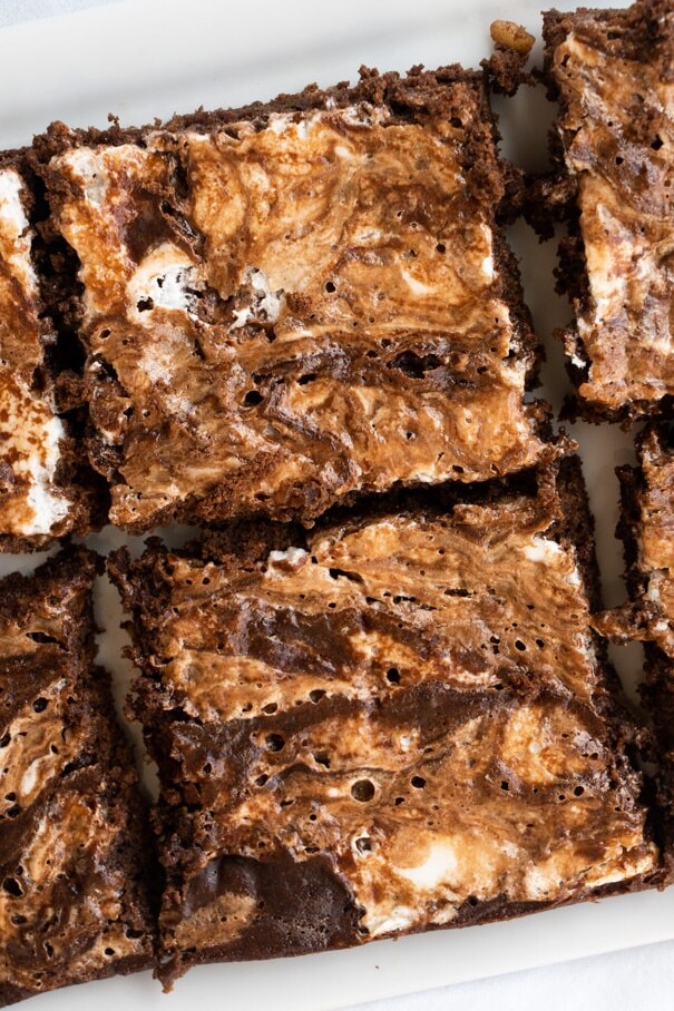 Close-up of chocolate brownies with a marbled, swirled pattern of chocolate and white cream on top, cut into square pieces and arranged on a white surface.
