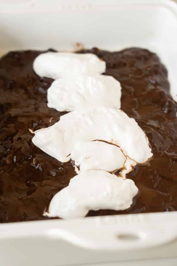A chocolate dessert in a white baking dish with five dollops of melted marshmallow or whipped topping arranged in a line down the center.