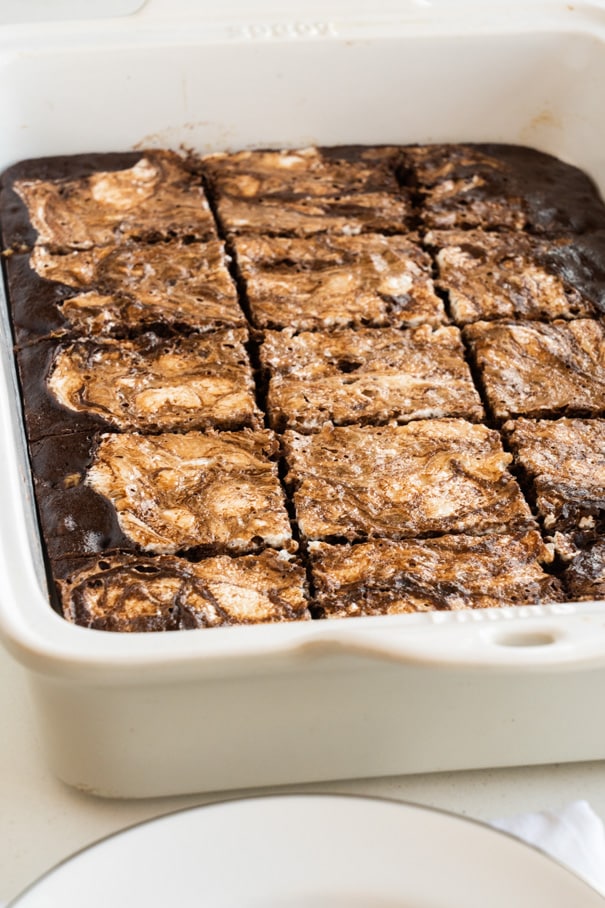 A white baking dish filled with chocolate brownies topped with a marbled swirl, cut into squares and ready to serve.