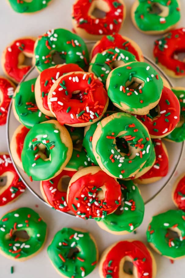 plate filled with christmas cookies resembling mini donuts with icing and sprinkles.