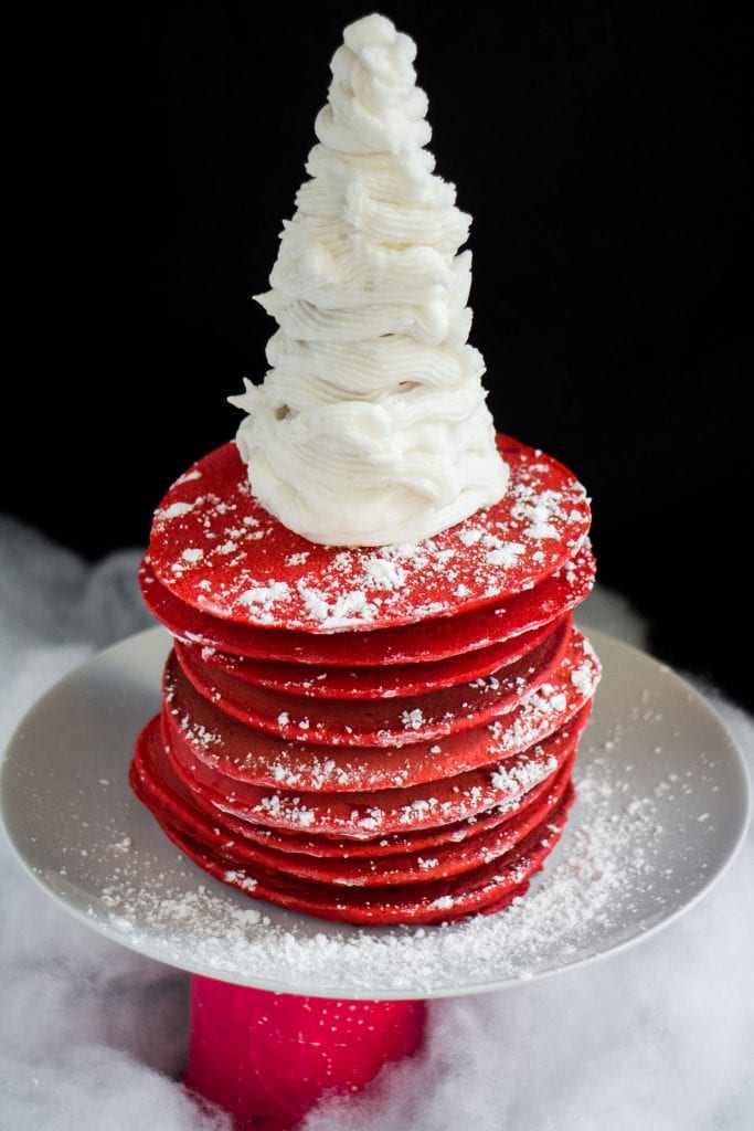 red pancakes with powdered sugar and frosting on them, sitting on white plate
