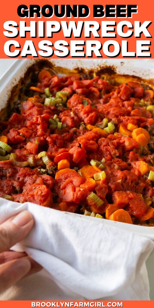 A baked casserole dish filled with ground beef, chopped carrots, celery, and diced tomatoes. A hand holds a white towel, partially uncovering the dish. Bold text above reads Ground Beef Shipwreck Casserole.