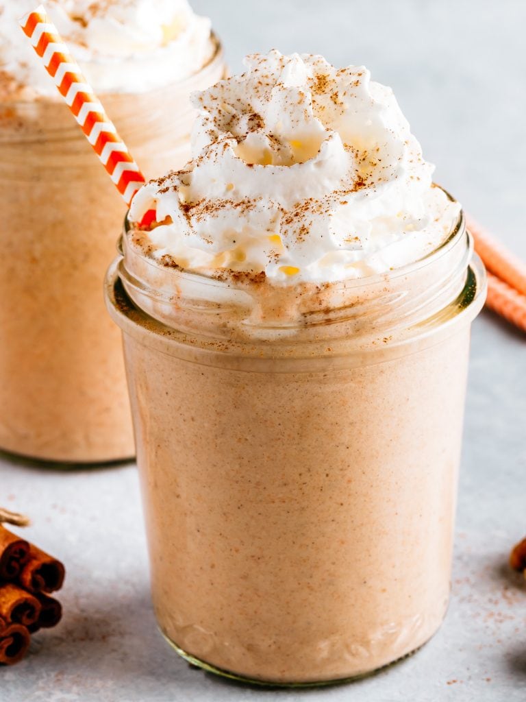 pumpkin pie milkshake in glass jar with whipped cream on top and red straw.