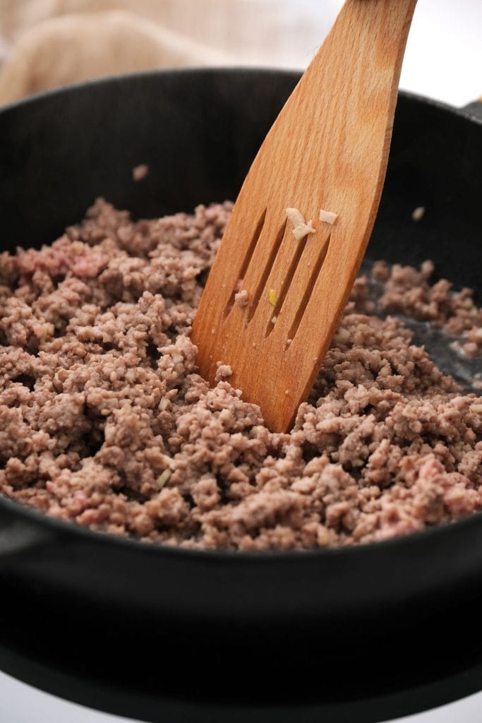 ground beef browning in frying pan on top of oven.